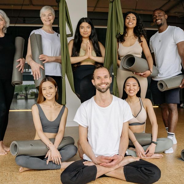 A diverse group of people smiling in a calm yoga studio setting.